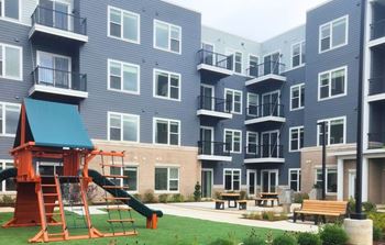 A playground area with a slide and picnic tables is in front of a building.